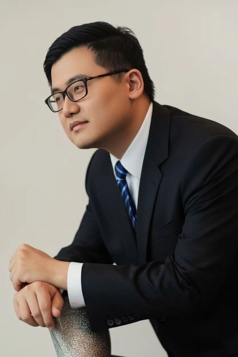 Man in suit and glasses posing thoughtfully.